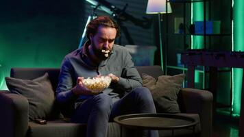 Man in apartment chocking on food while watching movie on TV and eating popcorn. Person getting throat clogged while swallowing snack, doing heimlich maneuver on couch, fighting for his life, camera A video