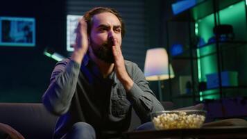 Upset man throwing popcorn at TV screen, watching football competition live on TV, reacting in anger to goal scored by opposing team. Sports fan at home annoyed by refereeing mistake, camera A video