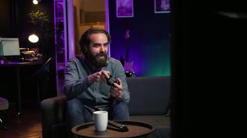 Focused man playing videogame in neon illuminated home, holding controller. Gamer hooked on enthralling game, excited to participate in online tournament, battling other players, camera B video
