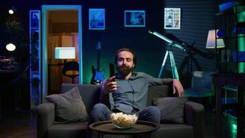 man använder sig av avlägsen till växla kanaler på tv skärm, känsla frustrerad förbi ointressant innehåll. uttråkad person rullning genom TV kanaler, upprörd efter inte upptäckt något kan ses, kamera b video