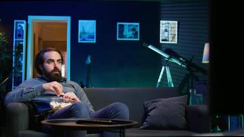 Man at home shocked by thriller film ending on TV, dropping popcorn out of mouth. Stupefied person at home left with eyes wide open by dramatic plot twist, watching suspenseful movie on TV, camera B video