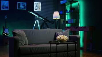 Cozy residential interior with sofa and snack setup, ready for casual movie night or immersive TV viewing experience. Bowl of popcorn on table in neon illuminated home theater apartment video