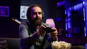 Excited man playing videogames using controller, having fun in neon illuminated room. Enthusiastic gamer competing in multiplayer game using gamepad, talking with friends through headset, camera A video