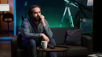 Man at home shocked by thriller film on TV, drinking coffee. Stupefied person at home left with eyes wide open by dramatic plot twist, watching suspenseful movie on TV, enjoying beverage, camera A video