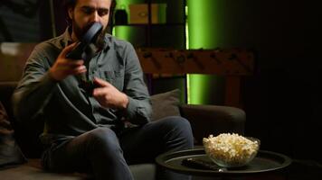 Smiling man putting headphones on to play videogames on gaming console with teammates. Happy player enjoying defeating foes in game, discussing with friends through headset, camera A video