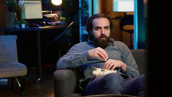 Man at home looking in disbelief at thriller film on TV, stuffing mouth with popcorn. Stupefied person at home watching suspenseful movie on VOD channel, perplexed by plot twist, camera A video