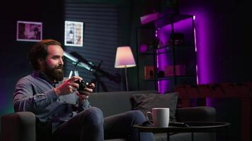 Man enjoying playing videogame in neon lit room, holding controller. Gamer participating in internet esports competition using professional gamepad for better victory chances, camera B video
