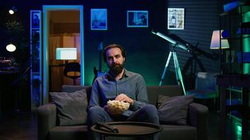 Sad man sitting on couch feeling heartbroken while watching tragic movie on streaming service. Depressed person seeing TV show favorite character dying, showing emotional discomfort, camera B video