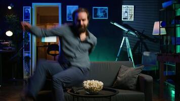 Excited man throwing himself on couch, rushing to catch start of favorite TV show episode. Enthusiastic person in a hurry to watch television series jumping on couch at home, camera B video