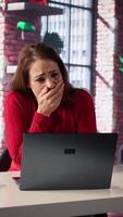 Vertical Exhausted woman trying to solve daily tasks on laptop at home office, struggling to pay attention to remote freelance work. Person yawning and being overworked surfing the web. Camera B. video