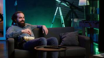 Joyous homeowner using TV to watch comedy films on streaming services, laughing at funny jokes. Radiant man in home theater consuming entertainment, amused by humorous movie scene, camera A video