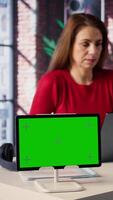 Vertical Mature woman reading forms and papers next to isolated screen and studying handwritten notes, surfing the web and staying connected for her freelance work tasks. Multitasking online. Camera B. video
