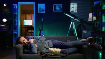 man om ner kramas kudde tittar på tv, förtvivlad förbi upprörande film komplott. ledsen visare lounged på soffa i rgb upplyst lägenhet, upprörd förbi deprimerande tv visa scen, kamera b video