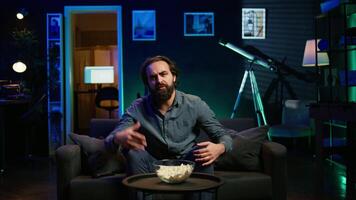 Disappointed supporter watching sports match on live broadcast, upset by team mistake. Annoyed man at home on couch looking at football competition, dejected by chance missed by player video