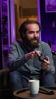 Vertical Focused man playing videogame in neon illuminated home, holding controller. Gamer hooked on enthralling game, excited to participate in online tournament, battling other players, camera B video