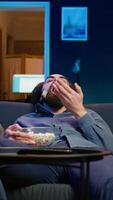 Vertical Bored man at home entertaining himself by throwing popcorn in air and catching it with mouth, wasting time. Person slacking off, eating salty snacks and lounging on couch watching TV, camera B video