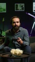 Vertical Smiling man putting headphones on to play videogames on gaming console with teammates. Happy player enjoying defeating foes in game, discussing with friends through headset, camera B video