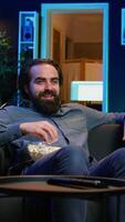Vertikale freudig Hausbesitzer mit Fernseher zu Uhr Komödie Filme auf Streaming Dienstleistungen, Lachen beim komisch Witze. strahlend Mann im Zuhause Theater verbrauchen Unterhaltung, amüsiert durch humorvoll Film Szene, Kamera b video