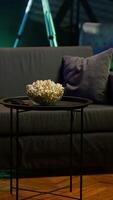 Vertical Snack and remote on coffee table in home room with dimmed lighting creating relaxed mood for movie night, close up. Panning shot of popcorn bowl on table in neon lit modern apartment video