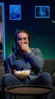 Vertical Man in apartment chocking on food while watching movie on TV and eating popcorn. Person getting throat clogged while swallowing snack, doing heimlich maneuver on couch, fighting for his life, camera B video