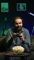 Vertical Excited man holding controller in neon illuminated apartment, playing videogames. Happy gamer on couch using joystick to participate in PvP game on console system, relaxing and having fun, camera B video