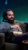 Vertikale freudig Hausbesitzer mit Fernseher zu Uhr Komödie Filme auf Streaming Dienstleistungen, Lachen beim komisch Witze. strahlend Mann im Zuhause Theater verbrauchen Unterhaltung, amüsiert durch humorvoll Film Szene, Kamera ein video