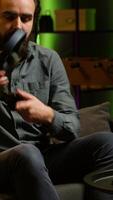 Vertical Smiling man putting headphones on to play videogames on gaming console with teammates. Happy player enjoying defeating foes in game, discussing with friends through headset, camera A video