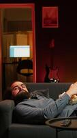 Vertical Gamer lounged on couch focused on winning competitive multiplayer game eating popcorn. Person in home theatre holding controller munching on salty snack, playing videogames, camera B video