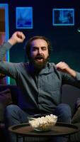 Vertical Ecstatic sports fan watching live match broadcast at home, shouting to celebrate favorite team scoring. Euphoric man yelling, doing frantic hand gesturing, delighted about goal, camera B video