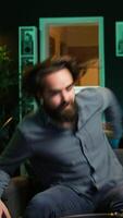 Vertical Cheerful gamer rushing home to play newly released game. Happy man jumping on couch, eager to play videogame on console, relaxing after hard day at work, camera B slow motion shot video