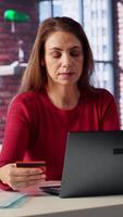 Vertical Smiling lady holds her card while she pays for the online order, using tablet at home office to transfer money and make a purchase. Pleased woman shopping after checking credit balance. Camera A. video