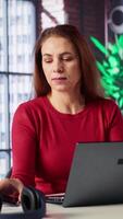 Vertical Female freelancer at home calling her team members to discuss online research and surfing the internet, utilizing a laptop for telework. Staying connected on telephone line call. Camera A. video