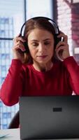 Vertical Tech savvy user working on a laptop and listening to focus music at home, enjoying freelancing tasks and multitasking. Cheerful woman having fun with great rhythm, productive lifestyle. Camera A. video