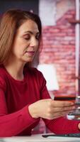 Vertical Relaxed woman entering card numbers to verify the balance before paying online, e commerce on webpages from the home desk. Person making web transactions and transferring money. Camera A. video