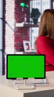 Vertical Freelancer does research by reading articles and papers next to chroma key display, collecting information for new project. Woman multitasking and studying files with handwritten notes. Camera B. video