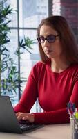 Vertical Mature person overseeing business schedule and planning activities at desk, working on time management with digital tools. Female freelancer utilizing the pc and multitasking. Camera B. video