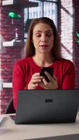 Vertical Focused woman in a home office loft talking on a mobile phone while working on laptop. She juggles calls, meetings and inquiries, using communication skills and creativity to solve tasks. Camera B. video