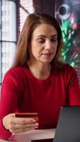 Vertical Relaxed woman entering card numbers to verify the balance before paying online, e commerce on webpages from the home desk. Person making web transactions and transferring money. Camera B. video