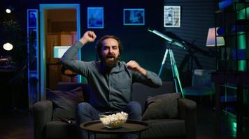 Ecstatic sports fan watching live match broadcast at home, shouting to celebrate favorite team scoring. Euphoric man yelling, doing frantic hand gesturing, delighted about goal, camera B video