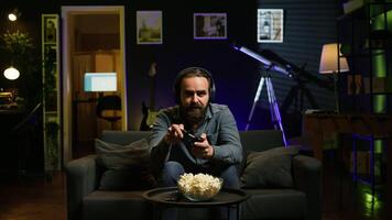 Man looking in disbelief at TV screen while playing videogames, receiving game over message on gaming console. Gamer upset after being defeated by rival players in online esports competition, camera B video