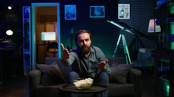 Supporter watching sports match on live broadcast, raging on couch in anger seeing team mistake. Angry man looking at football competition fuming, releasing pent up emotions, camera B video