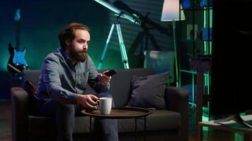 Man appalled by upsetting breaking news story on TV, doing phone call to family member. Person at home scared by troubling events broadcasted on TV, calling friend using smartphone, camera A video