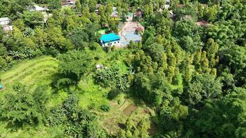 using a drone that shows a small villa-like building with a badminton court in front of it. The surrounding area is covered with lush green trees and land. video