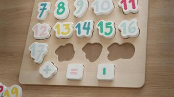 the boy learns to count, holds a board with numbers-puzzles arranged in order from 1 to 20, the boy is 4-5 years old European appearance, at home sits at the table, preparation for school video
