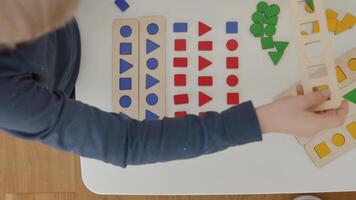 The child carefully arranges the red and blue wooden geometric shapes circle, square, triangle and rectangle on the table, sorting them by shape. A wonderful Montessori-inspired learning experience. video