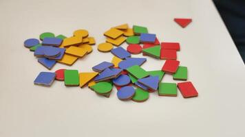 flat wooden geometric figures circle, square, triangle, rectangle of different colors - yellow, blue, green, red - are scattered on the table, the boy mixes them up video