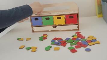 The little pupil places multicolored geometric shapes into the corresponding boxes. red, yellow, green and blue. geometric shapes of different colors are scattered on the table. This Montessori video