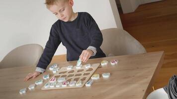 the boy learns to count, holds a board with numbers-puzzles arranged in order from 1 to 20, the boy is 4-5 years old European appearance, at home sits at the table, preparation for school video