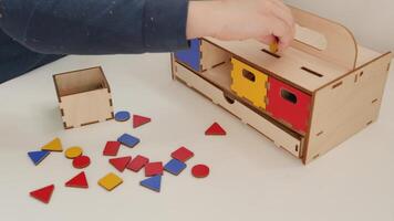 A little pupil arranges multicolored geometric shapes in a chest with multicolored boxes. red, yellow, green and blue. geometric shapes of different colors are scattered on the table. This Montessori video