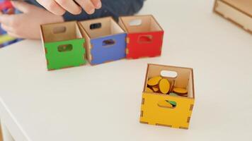 A childs hands sort flat geometric shapes by color into four boxes. red, yellow, green, and blue. A fun educational activity for developing logical thinking, color recognition, and fine motor skills video
